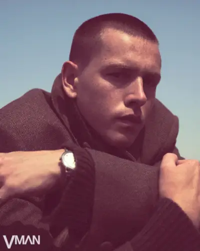 Harris Dickinson nosi prevelik plašč v obliki ribje kosti in majico Givenchy iz kašmirja z uro OMEGA De Ville Prestige.