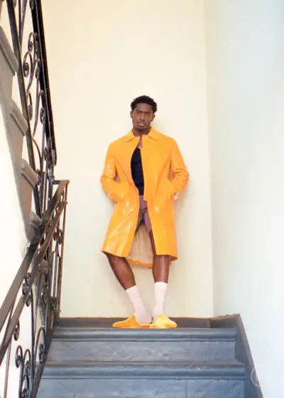 ダムソン・イドリスは、カルバン・クラインのトップにルアーのショートパンツ、ランバンの黄色のコート、そしてレニス・ワールドのスリッパを着ています。