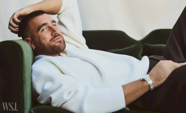 Travis Kelce descansa casualmente con un suéter blanco, yuxtapuesto con el rico verde de una silla de terciopelo, para WSJ. Revista.