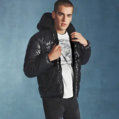 Jake Hart schlüpft in eine Wendejacke von Buffalo David Bitton und präsentiert dazu ein grafisches T-Shirt und schwarze Jeans im Used-Look der Marke.