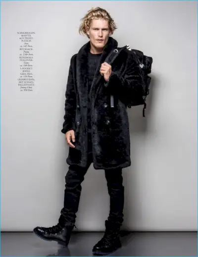 Modelul englez Harry Goodwins pune un picior înainte, purtând cizme Jimmy Choo, o haină ASOS, rucsac Prada, pulover Gant și blugi Calvin Klein.