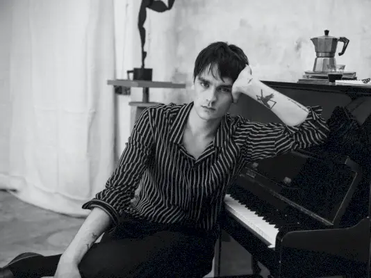 Alain-Fabien Delon, pózujúci proti klavíru, má pruhovanú košeľu s nohavicami značky Mango Man.