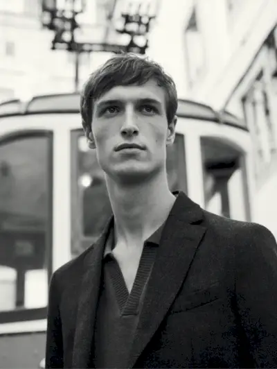 Apărând într-o fotografie alb-negru, Egon Van Praet poartă un pulover polo cu decolteu în V și un blazer de flanel de lână slim-fit de la Massimo Dutti.