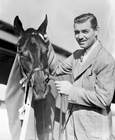 Clark Gable porte un costume de couleur claire avec un pull à col en V alors qu'il pose avec son cheval Beverly Hills dans son ranch vers le 21 avril 1937.