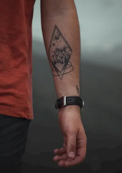 Denne tatovering på underarmen kombinerer kunstfærdigt et fredfyldt landskab med et æterisk himmellegeme, hvilket antyder en kosmisk forbindelse.