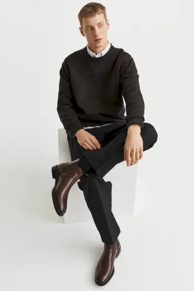 Lockern Sie Ihren schwarzen Anzug mit einem Pullover und braunen Chelsea-Stiefeln auf.