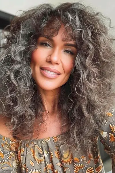 50歳以上の女性向けの前髪のあるナチュラルなカールのロングヘアスタイル。