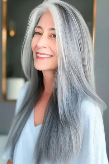 Dlouhý rovný šedý účes na usmívající se ženě kolem 60 let.