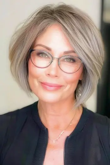 Krótka fryzura typu bob z przedziałkiem dla kobiet po 50. roku życia w okularach.
