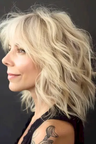 60歳以上の女性のためのチョッピーブロンドのシャグミディアムレングスのヘアスタイル。