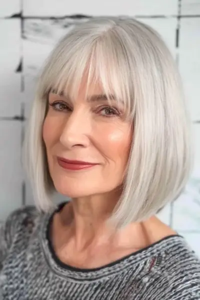 60歳以上の女性のための前髪のあるシルバーのブラントボブ、ミディアムレングスのヘアスタイル。