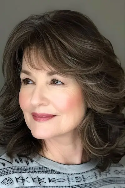 前髪のある50歳以上の女性のためのミディアムレングスのフェザーレイヤーのヘアスタイル。