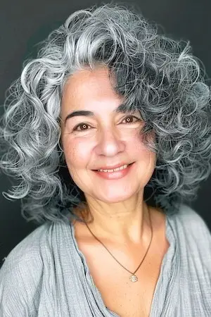 둥근 얼굴을 가진 50세 이상 여성을 위한 볼륨감 있는 회색 컬 헤어스타일.