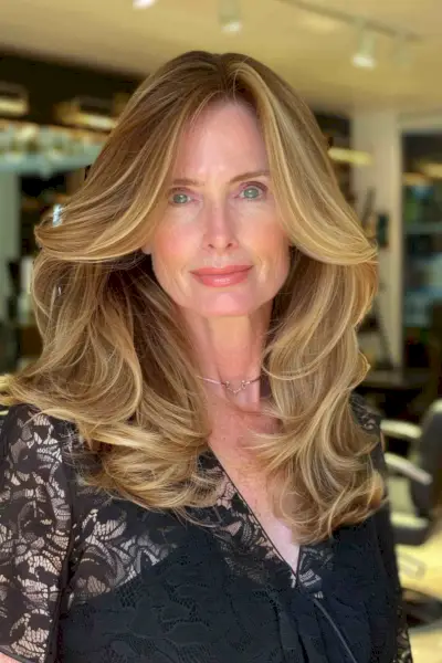 Woman with medium-length voluminous hair, featuring soft waves and a side part, suitable for oval faces.