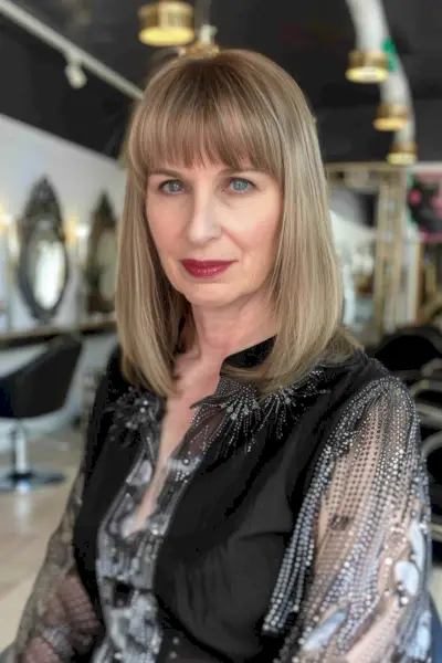 Woman with medium-length hair and straight bangs, featuring a polished, sophisticated look.