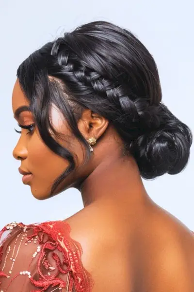 サイドにスイープした三つ編みと低いお団子の黒いプロムのヘアスタイルのアイデア。