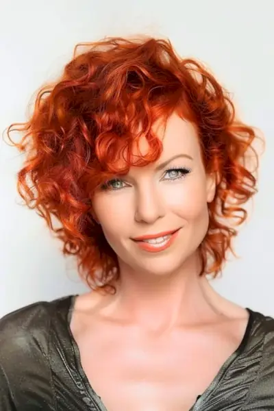 Acconciatura riccia con ricci color rame vivido per donne sopra i 50 anni.