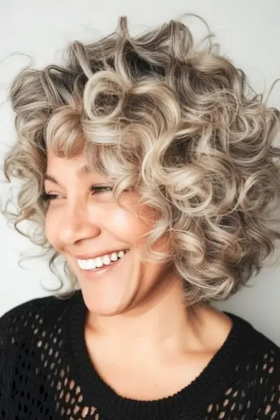 Acconciatura riccia con riccioli corti e voluminosi per donne sopra i 50 anni.