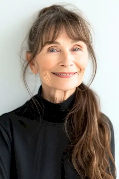 モックタートルネックを着た60歳以上の笑顔の女性にうっすら前髪のあるポニーテール。