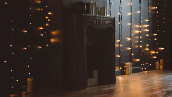 black mantel with twinkly lights and candles along wall next to it. 