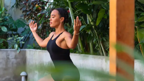 woman in black yoga outfit poses in front of lush palm trees and cement half wall